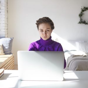 Kobieta w swoim pokoju pracuje przy laptopie. Praca zdalna - jak wpływa na wybór mieszkania?