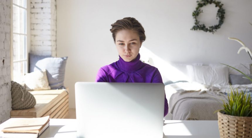 Kobieta w swoim pokoju pracuje przy laptopie. Praca zdalna - jak wpływa na wybór mieszkania?