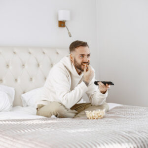 Mężczyzna na łóżku ogląda TV. Mieszkanie dla singla