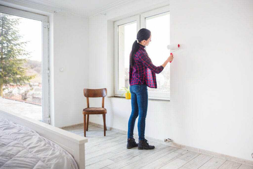 Kobieta maluje ścianę w mieszkaniu. Jak zaoszczędzić na urządzaniu mieszkania